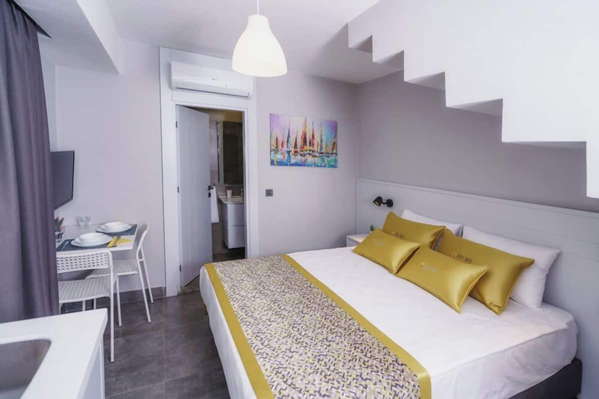 A hotel room with a bed, a desk, a chair, and a painting on the wall.