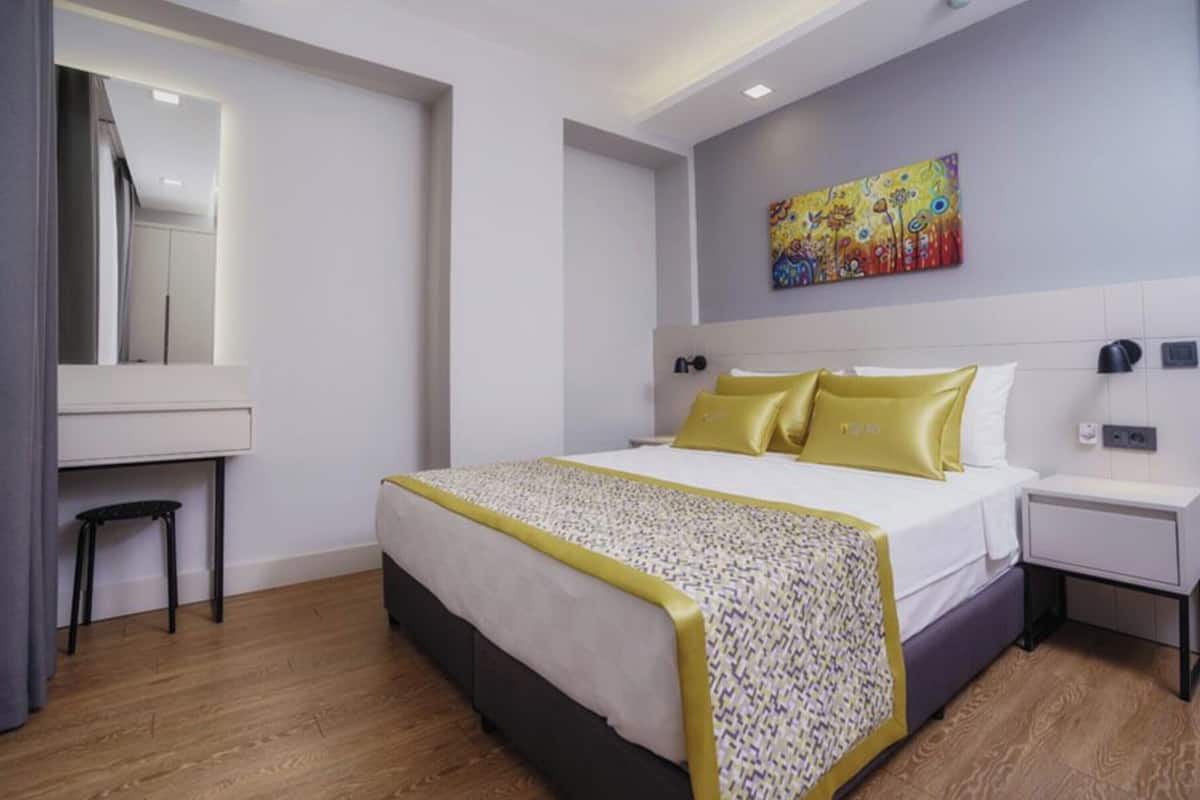 A hotel room with a bed, a desk, a chair, a painting on the wall, and a mirror.