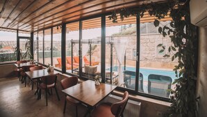 An indoor dining area with wooden tables and chairs, large windows, and a view of an outdoor swimming pool.