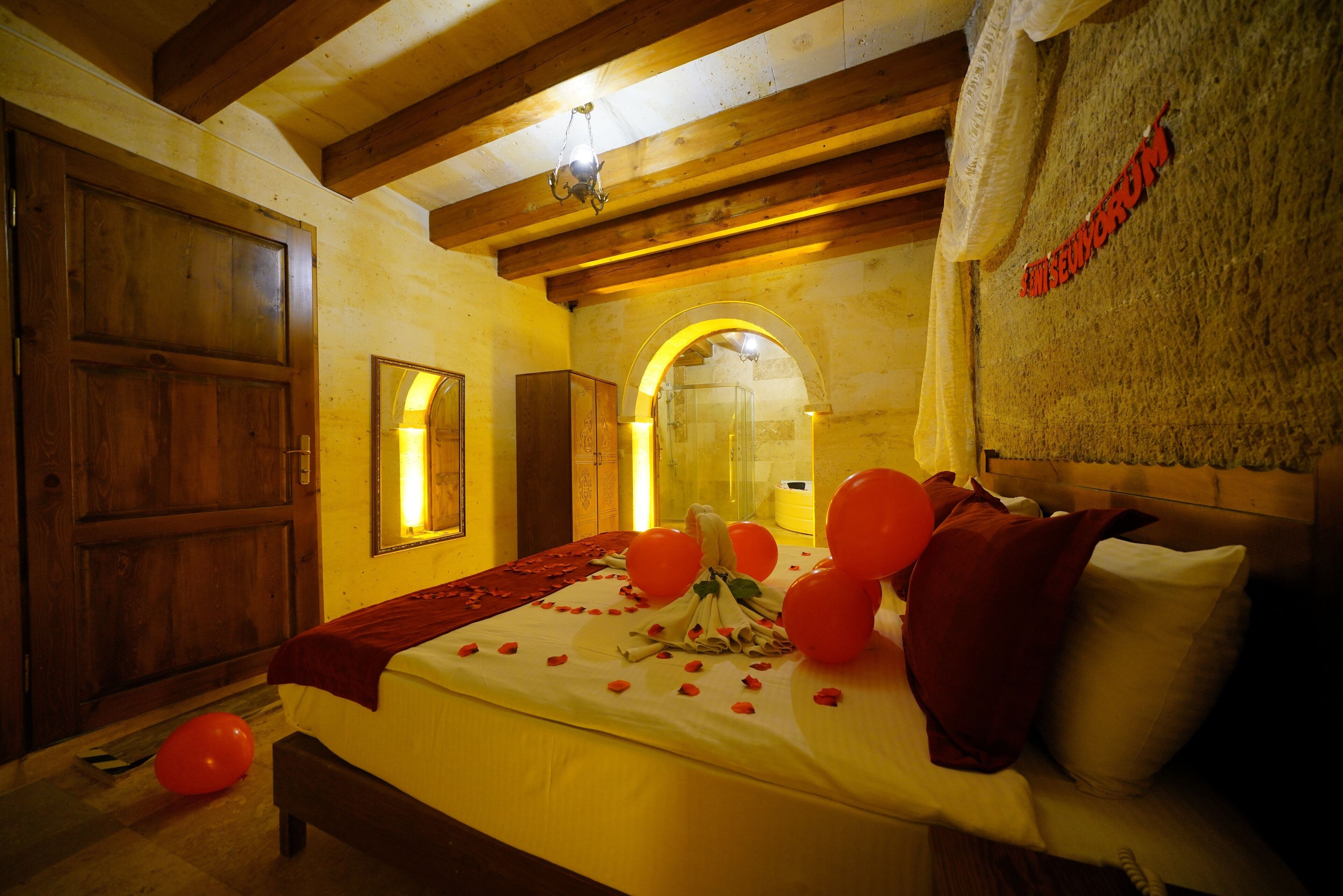 Habitación de hotel con techo de madera, una cama grande con almohadas rojas y blancas, y un cartel en la pared.