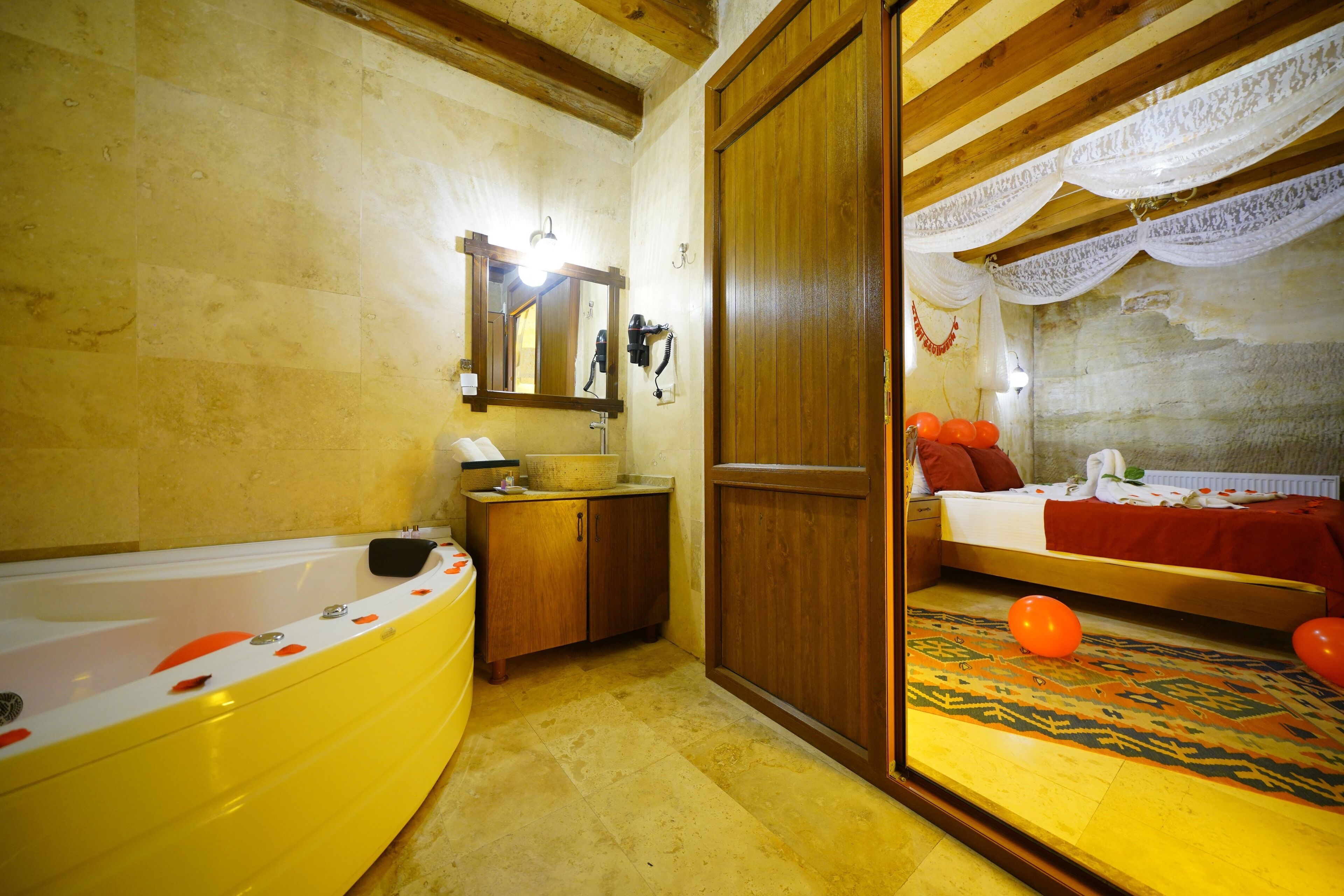 A bathroom with a bathtub, wooden cabinets, a mirror, and a bed with a patterned rug and balloons.