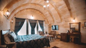 A bedroom with a bed, a desk, a chair, a television, and a fireplace.