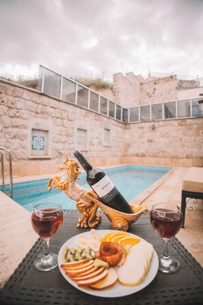 A poolside table with a bottle of wine, a golden horse statue, and a plate of fruit slices. - Balloon Cave Hotel (Nevsehir)
