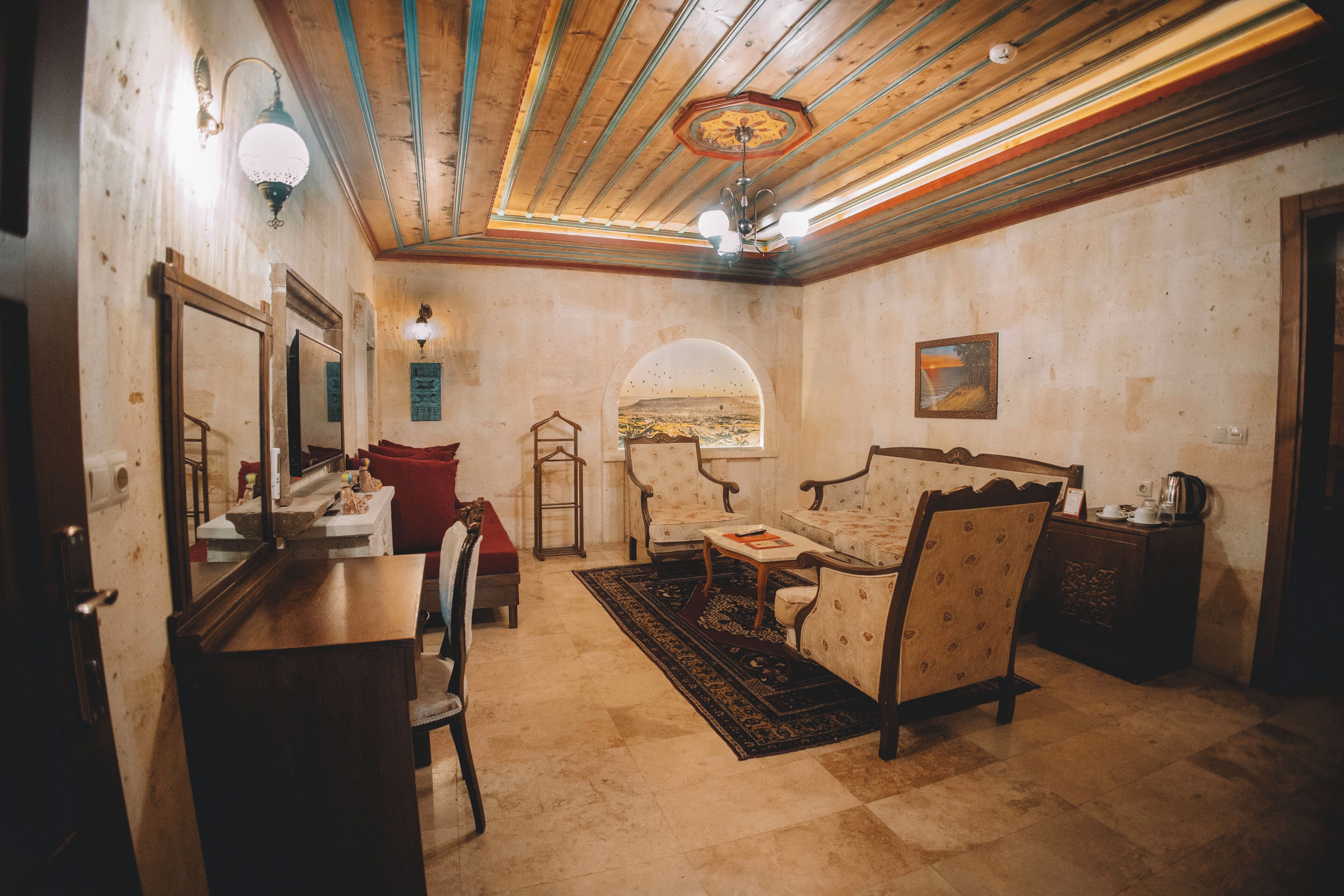 A room with a wooden ceiling, a large mirror, a sofa, a small table, and a view through an archway.