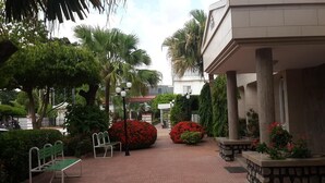 Un patio con bancos, palmeras y arbustos de flores rojas.