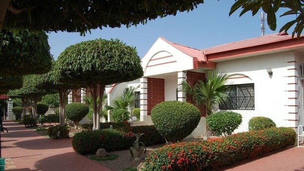 Un edificio de paredes blancas y techo rojo, rodeado de jardines y senderos bien cuidados.