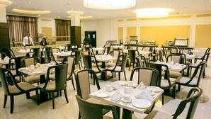 Un restaurante con varias mesas dispuestas para comer, una araña y un camarero uniformado.