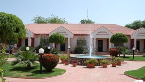 Un patio central con una fuente, rodeado de plantas en macetas y un edificio de techo rojo.