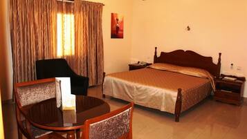 A hotel room with a bed, a chair, a table, and curtains.