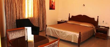 A hotel room with a bed, a chair, a table, and curtains.