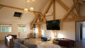 A spacious living room with a high ceiling, wooden beams, a flat-screen TV, and a cozy seating area with sofas and a rug.