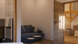 A modern room with a grey sofa, two small round tables, a wooden door, and a visible bed.