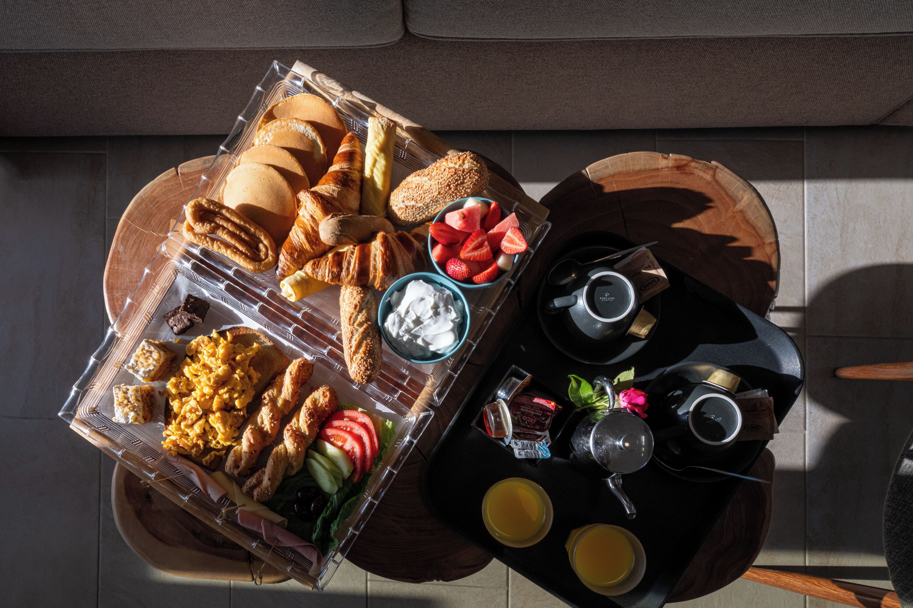 Een ontbijtplateau met croissants, roerei en vers fruit op een houten tafel.