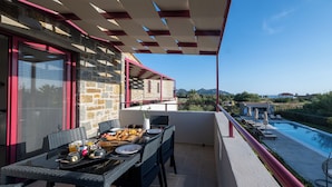 A balcony with a dining table set for breakfast, overlooking a swimming pool and a mountainous landscape. - Abeloessa Methonian Hospitality (Pylos-Nestoras)
