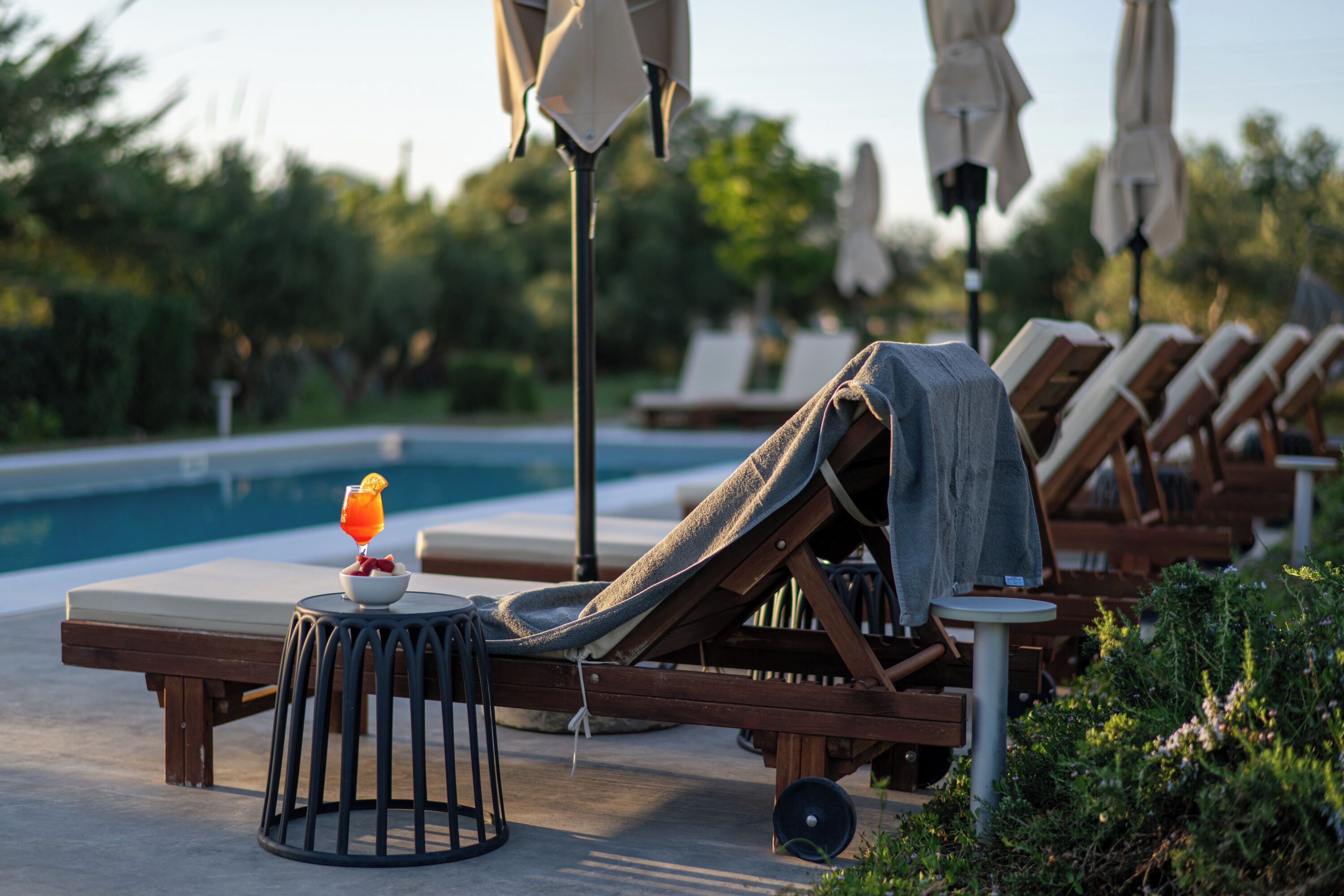 A poolside lounge area with sun loungers, a small table with a drink, and umbrellas.