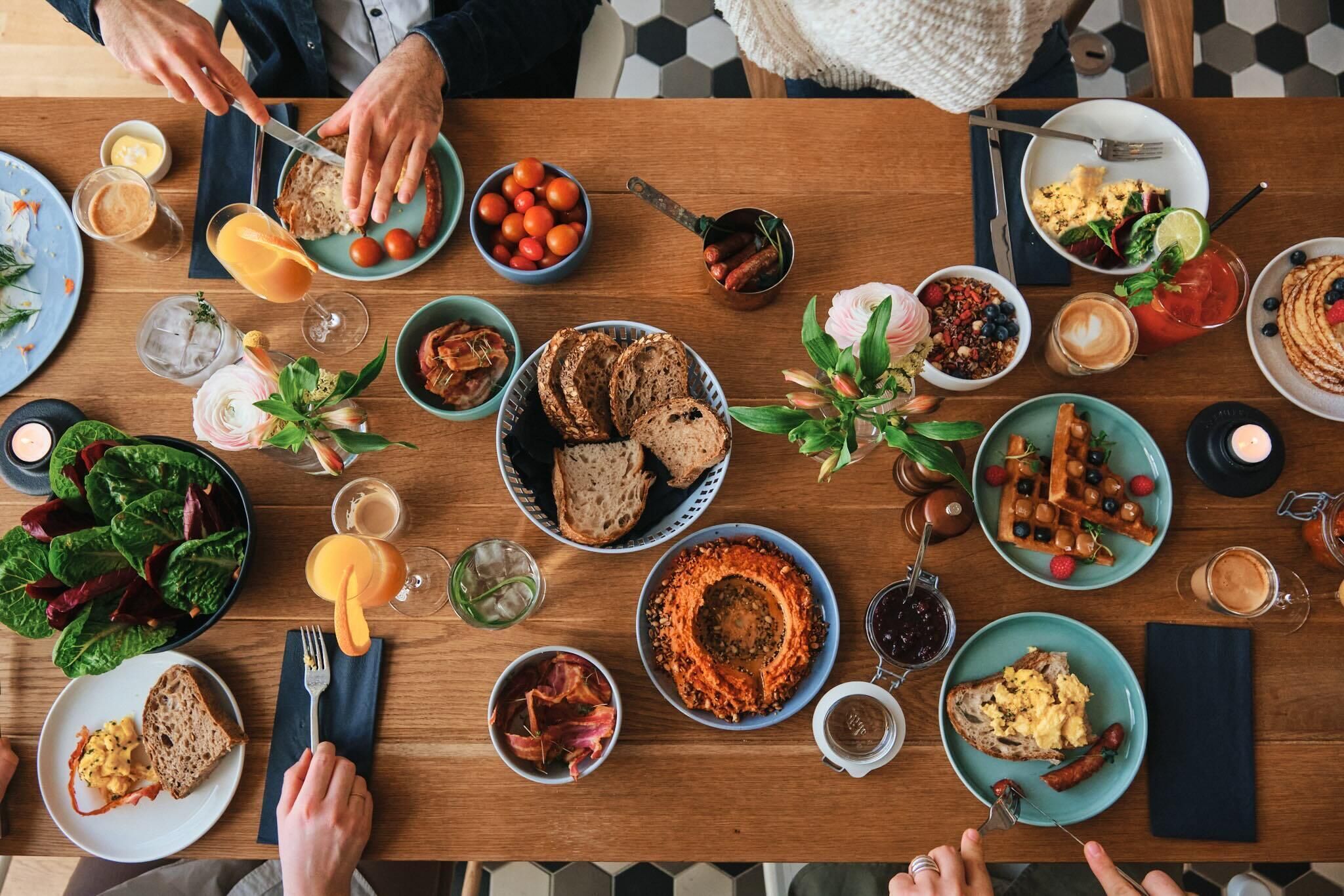 Une table en bois sur laquelle sont disposés divers aliments pour le petit-déjeuner, notamment des toasts, des œufs, des saucisses et une salade.