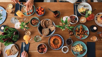 Une table en bois sur laquelle sont disposés divers aliments pour le petit-déjeuner, notamment des toasts, des œufs, des saucisses et une salade.