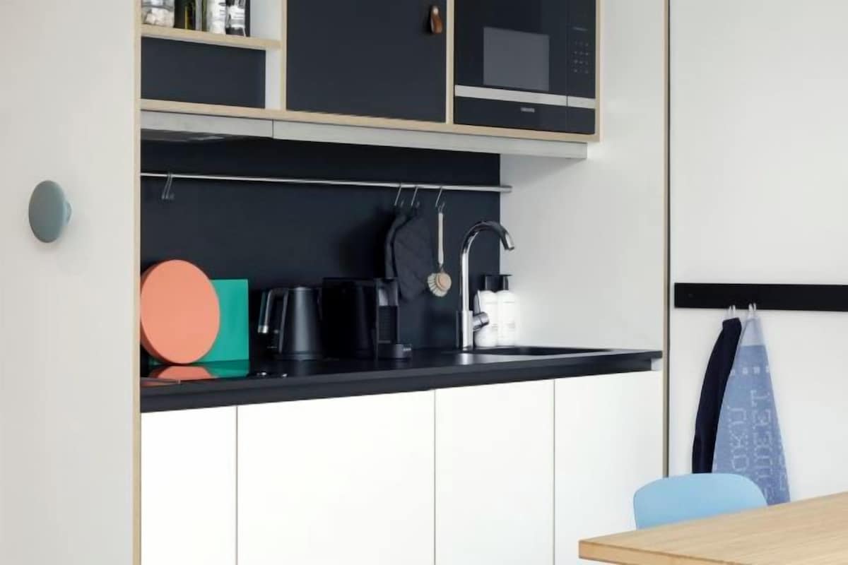 Una cocina moderna con encimera negra, armarios blancos y un microondas. Hay una cafetera, un hervidor y una toalla colgando.