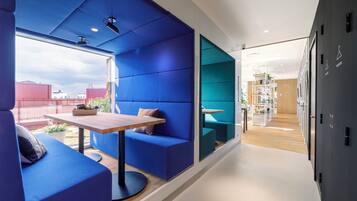 Un intérieur moderne avec un coin salon bleu, une table en bois et une vue sur le paysage urbain.