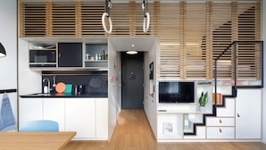 Een moderne keuken met inbouwapparatuur, een eethoek met een houten tafel en een trap met een televisie.