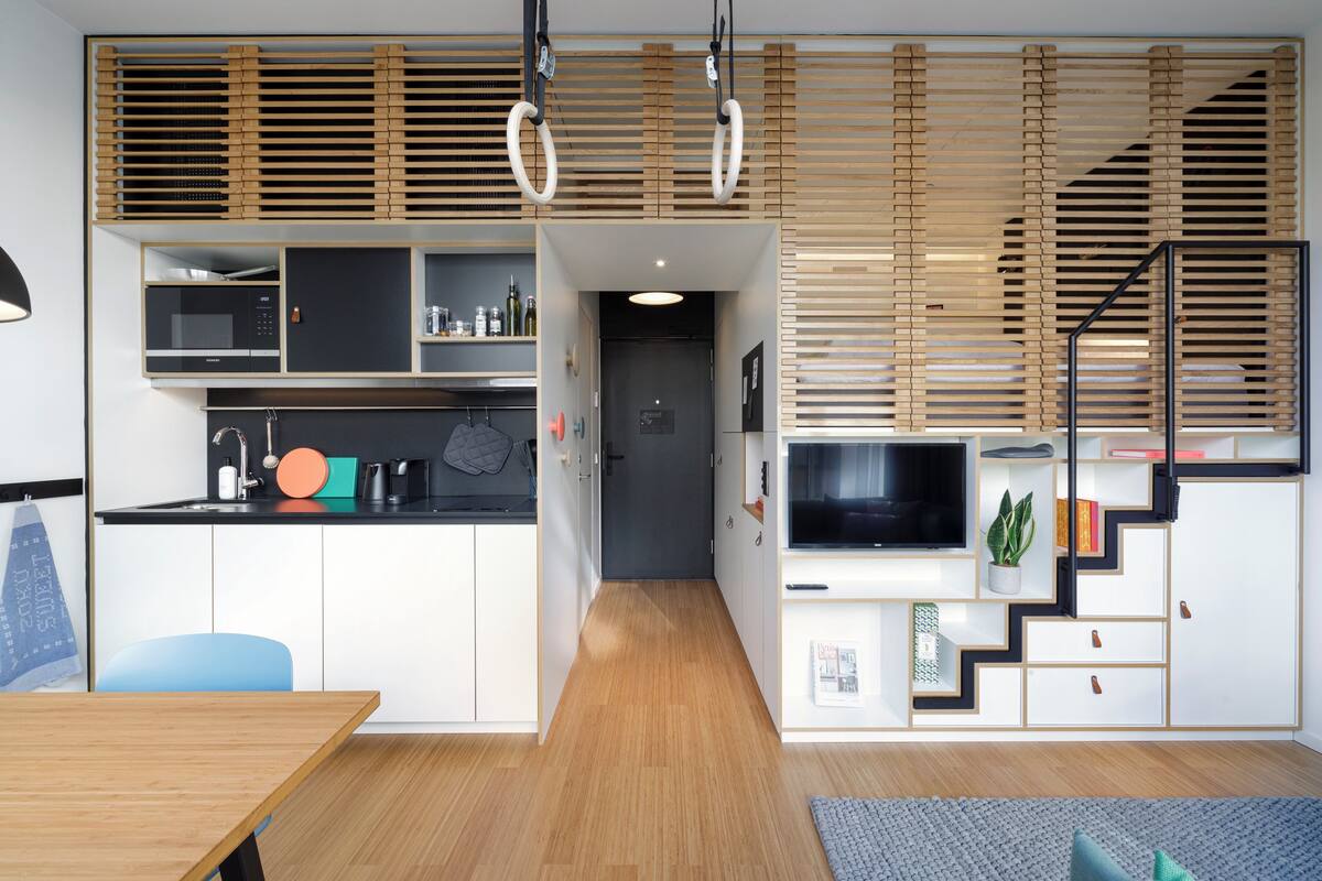 Een moderne keuken met inbouwapparatuur, een eethoek met een houten tafel en een trap met een televisie.