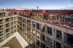 Un edificio moderno con varios pisos, amplias ventanas y una terraza en la azotea con mobiliario exterior.