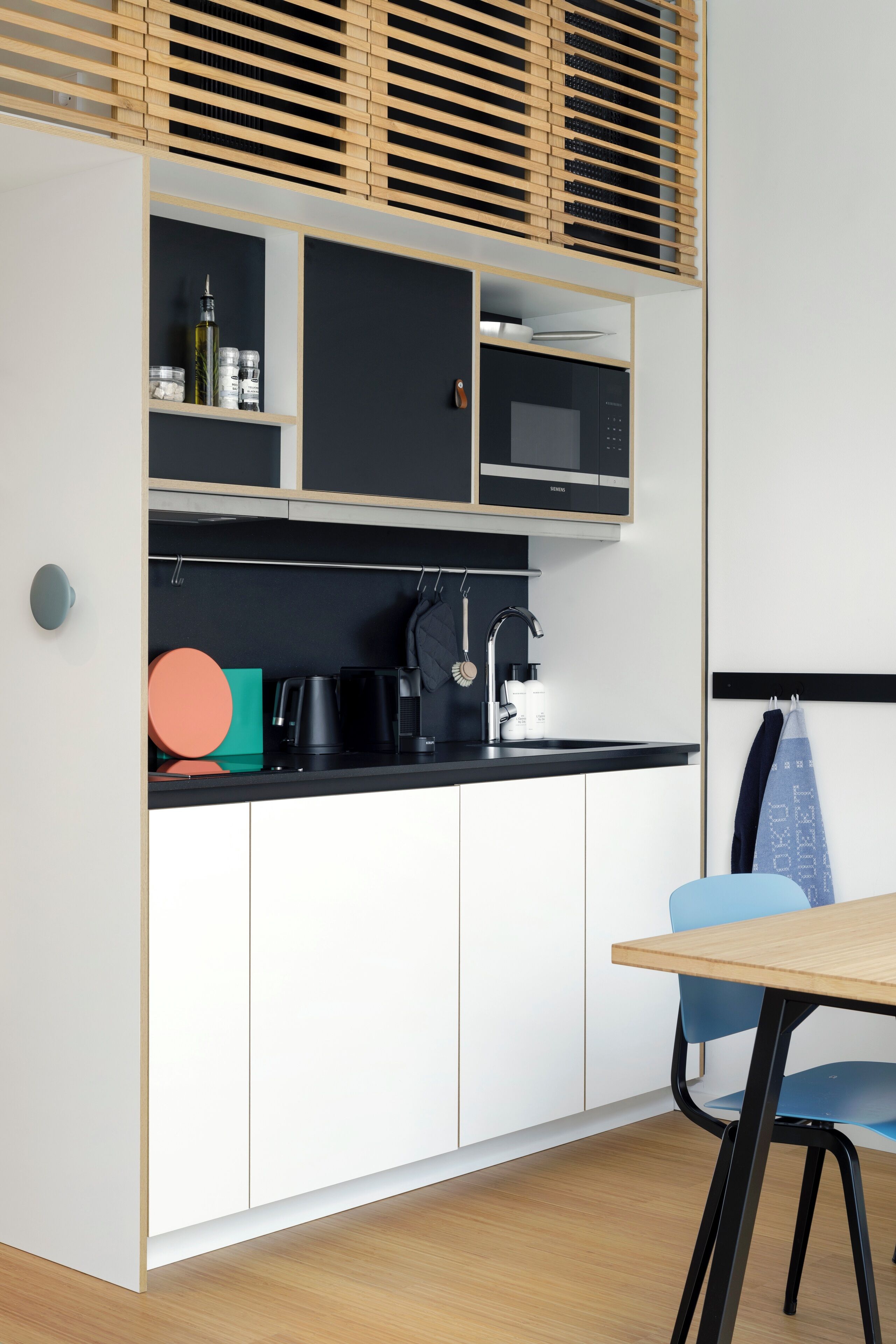 A modern kitchen with white cabinetry, a black countertop, and a wooden table.