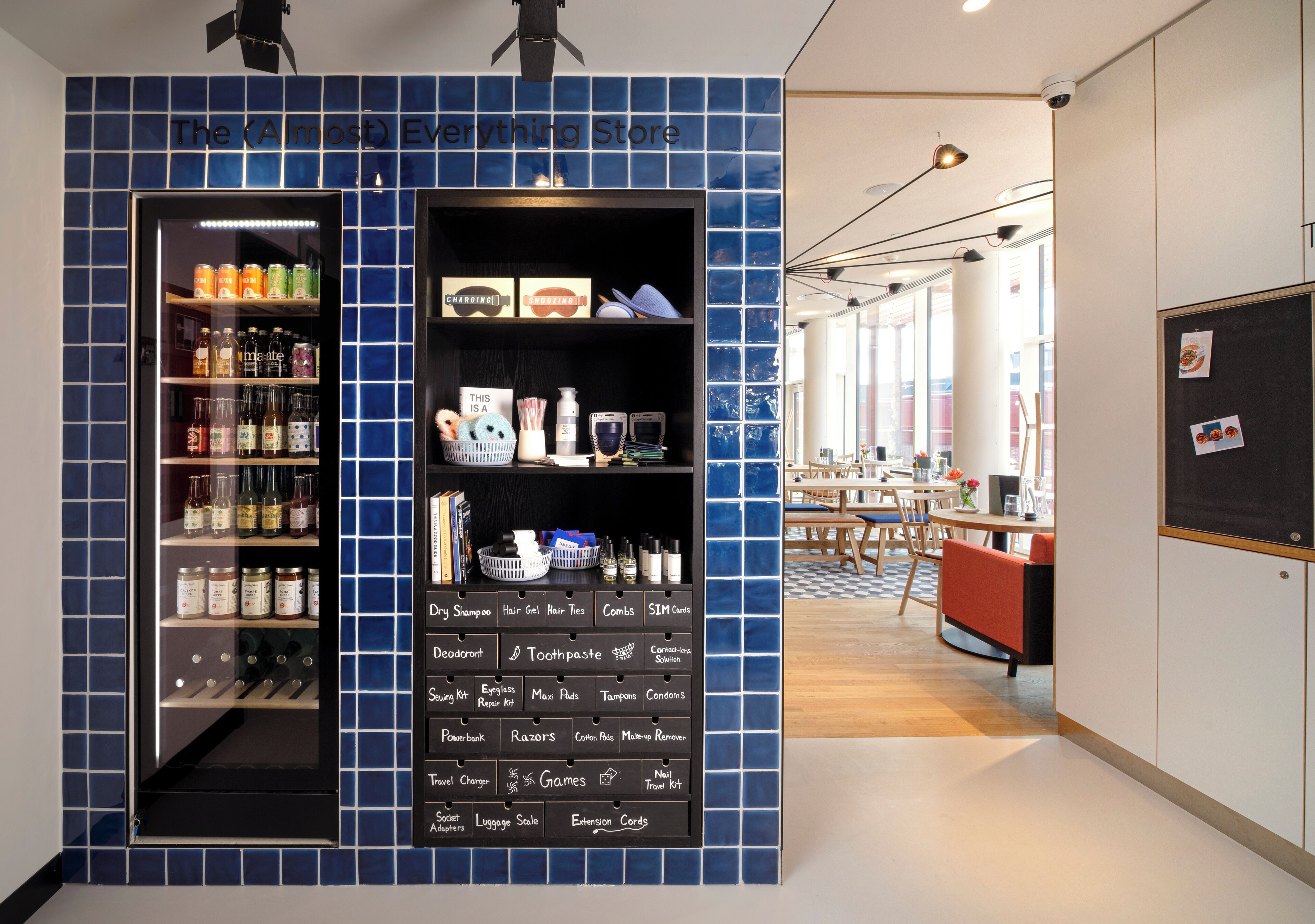 A store with a blue tiled wall, shelves of toiletries, and a chalkboard with product names.