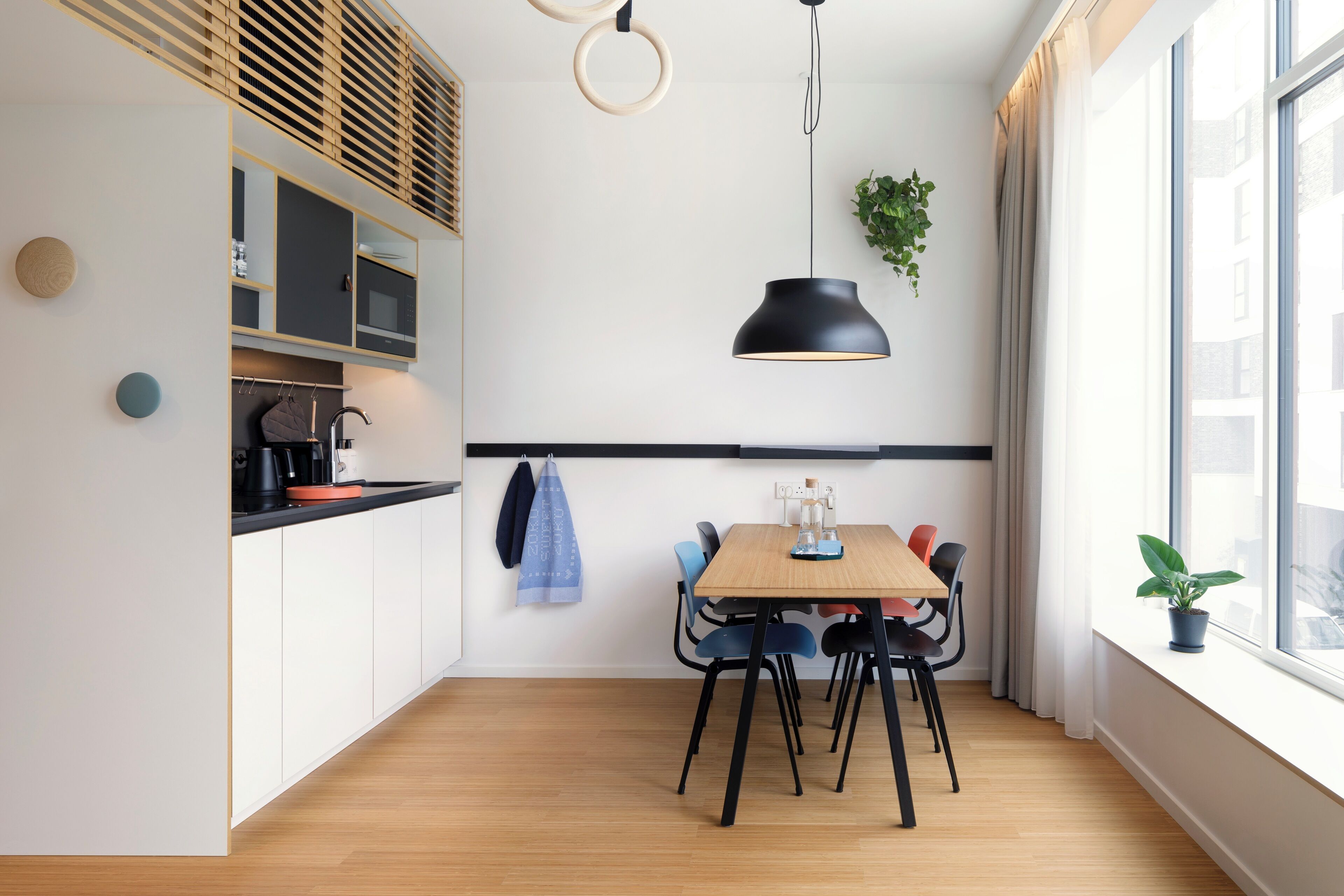 A modern kitchen with a dining area, wooden flooring, and a large window.