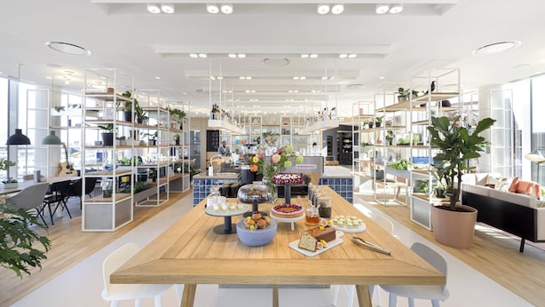 Een moderne, goed verlichte eetruimte met een houten tafel, witte stoelen en diverse gerechten en dranken.