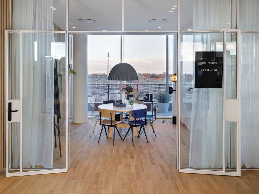 A modern dining area with a round table, chairs, and a view through large glass doors.