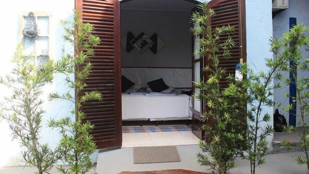 A small, cozy bedroom with a bed, wooden shutters, and a small balcony area. - Pousada Canto Azul (Guarujá)