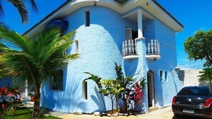 A blue house with a balcony, a car parked in front, and a palm tree. - Pousada Canto Azul (Guarujá)
