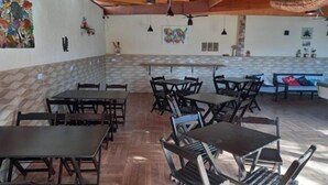 A spacious dining area with multiple tables and chairs, a high ceiling with exposed beams, and decorative wall art. - Pousada Canto Azul (Guarujá)