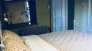 Une chambre à coucher avec un lit, une table de chevet avec une lampe, un radiateur, une fenêtre et une porte.