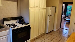 A kitchen with white cabinets, a gas stove, a refrigerator, and a tiled floor. - Serene Studio close to NYC. Walk to shops, PATH (Jersey City)