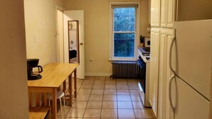 A narrow kitchen with a window, a radiator, and a wooden table with chairs. - Serene Studio close to NYC. Walk to shops, PATH (Jersey City)