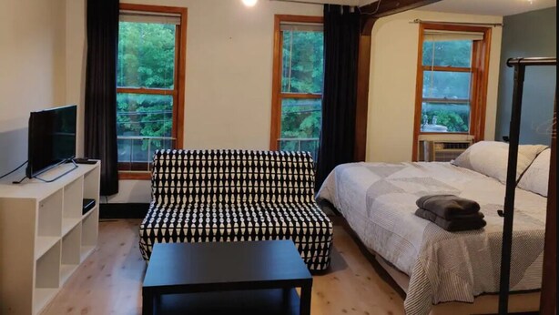 A bedroom with a bed, a sofa, a TV, and a ceiling fan. - Serene Studio close to NYC. Walk to shops, PATH (Jersey City)