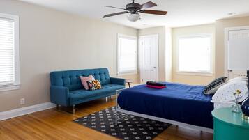 A bedroom with a bed, a blue sofa, a ceiling fan, and a small table with a lamp.