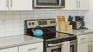 A kitchen with white cabinets, a stainless steel microwave, a black stove, and a blue kettle. - Luxury Building 3BR/2BA! Prime Downtown Mass Ave! (Indianapolis)