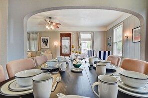 A dining room with a long table set for six, surrounded by chairs. There is a ceiling fan above the table, and the room has a neutral color palette with light walls. - Designer House 5BR! Steps to Downtown/Fountain Sq! (Indianapolis)