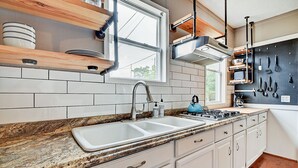 A modern kitchen with white cabinets, a granite countertop, a double sink, and a gas stove. - Designer House 5BR! Steps to Downtown/Fountain Sq! (Indianapolis)
