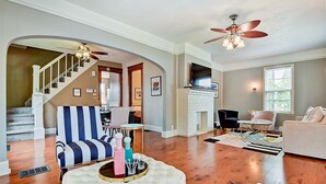 A spacious living room with hardwood floors, a striped armchair, a tufted ottoman, and a ceiling fan. - Designer House 5BR! Steps to Downtown/Fountain Sq! (Indianapolis)