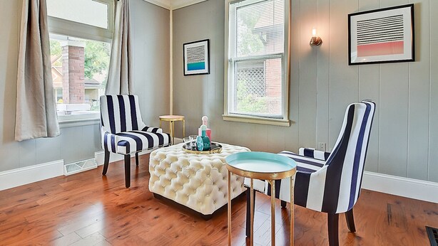 A room with a striped armchair, a tufted ottoman, and a small round table with a lamp. - Designer House 5BR! Steps to Downtown/Fountain Sq! (Indianapolis)