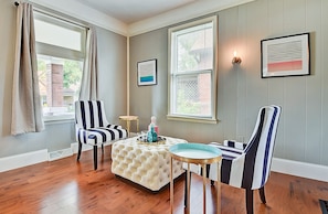 A room with a striped armchair, a tufted ottoman, and a small round table with a lamp. - Designer House 5BR! Steps to Downtown/Fountain Sq! (Indianapolis)