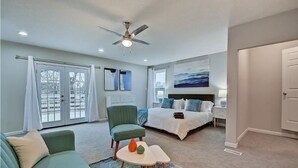 Une chambre à coucher moderne avec un lit, une chaise, une petite table et un ventilateur de plafond.