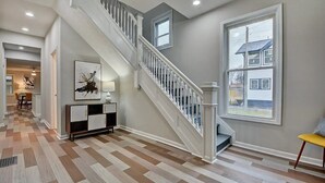 Un hall d’entrée spacieux avec un plancher en bois, un escalier doté de rampes blanches et une grande fenêtre donnant sur une maison.