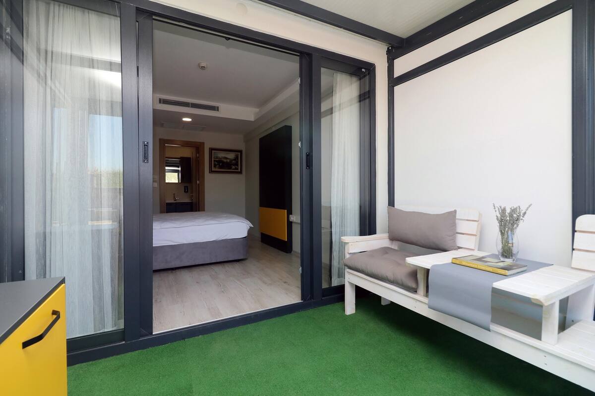 Ein modernes Hotelzimmer mit einem Bett, einer Couch, einem kleinen Tisch und einer Schiebetür zu einem weiteren Raum.