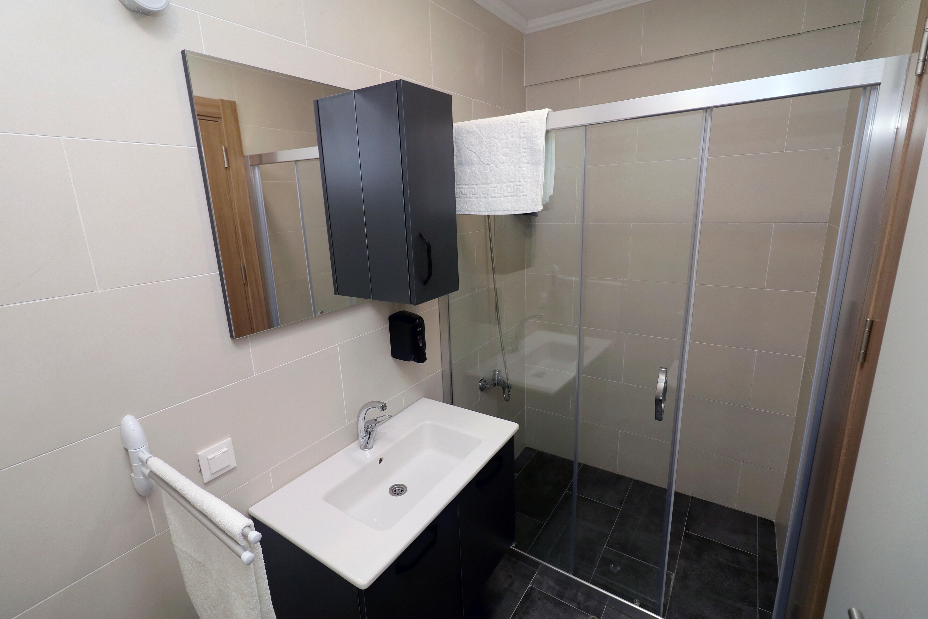 Un baño moderno con un lavamanos blanco, un mueble negro y una cabina de ducha de vidrio.