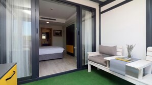 A modern hotel room with a bed, a sofa, a small table with a book, and a green carpet.